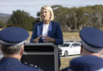 Woman in a blue blazer speaks at an outdoor press briefing behind a lectern, with police officers in the foreground.