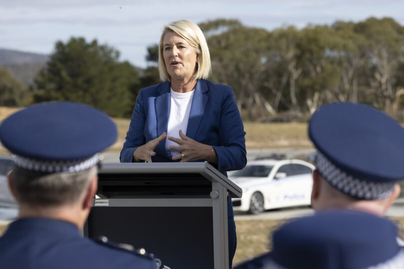 Woman in a blue blazer speaks at an outdoor press briefing behind a lectern, with police officers in the foreground.