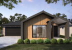 Modern single-story house with wood cladding, brick accents, large front window, and a covered entry amid landscaped greenery.