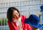 Woman in a red blazer high-fiving a child across a puzzle on a table outdoors