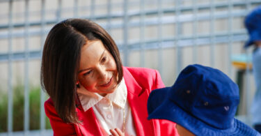 Woman in a red blazer high-fiving a child across a puzzle on a table outdoors