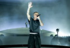 Lead singer on stage, microphone in hand, one arm raised, surrounded by fog and blue lighting.