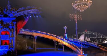 Ornate circus-style stage with gilded sculptures, red velvet curtains, and a blue-lit circular pool at night awaiting performance.