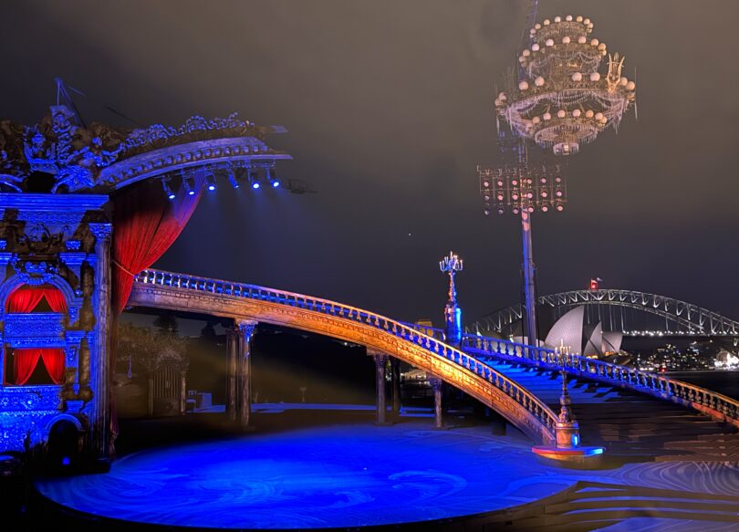 Ornate circus-style stage with gilded sculptures, red velvet curtains, and a blue-lit circular pool at night awaiting performance.