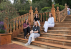Five friends pose for a photo on a terracotta-colored garden staircase with ornate railings, smiling at the camera.