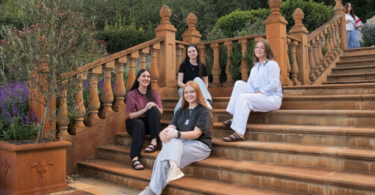 Five friends pose for a photo on a terracotta-colored garden staircase with ornate railings, smiling at the camera.
