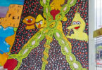 Vibrant mural on a stairwell wall with neon lime‑green looping chains, yellow cartoon characters, and a dotted black background.