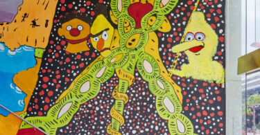Vibrant mural on a stairwell wall with neon lime‑green looping chains, yellow cartoon characters, and a dotted black background.