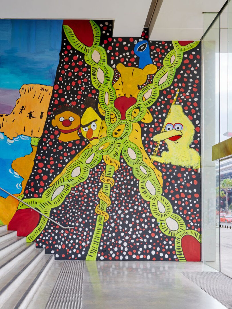 Vibrant mural on a stairwell wall with neon lime‑green looping chains, yellow cartoon characters, and a dotted black background.